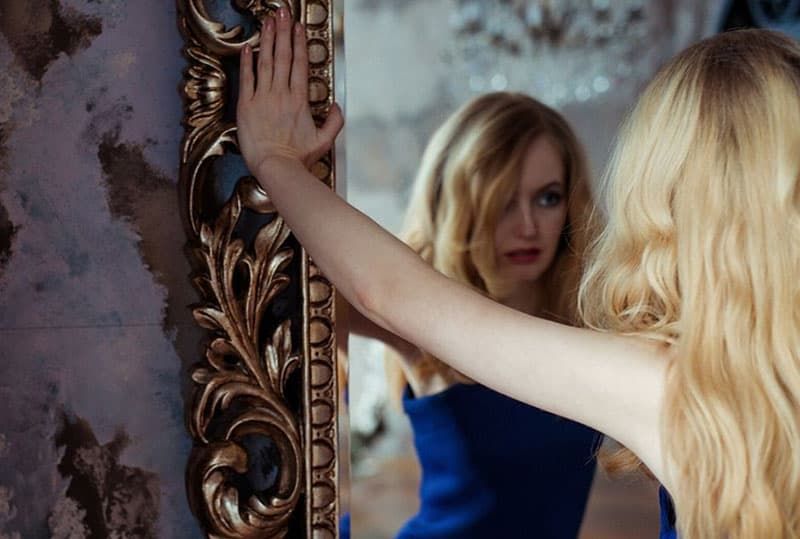 Nachdenkliche Frau vor einem Spiegel, die ein blaues Kleid trägt