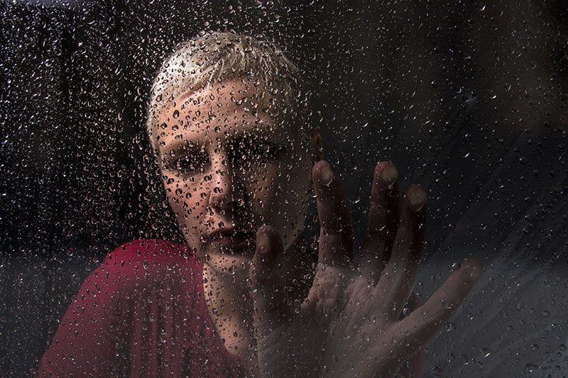Deprimierte Frau sitzt am regnerischen Glas