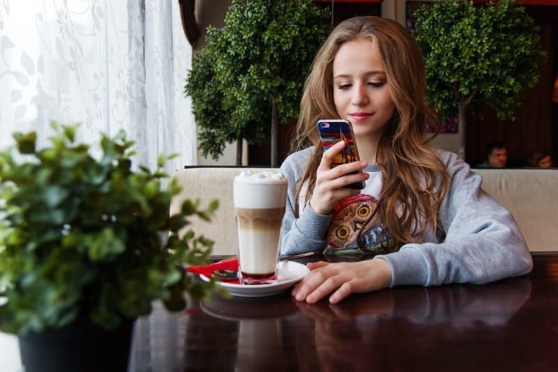 Frau benutzt Smartphone, während sie am Tisch sitzt