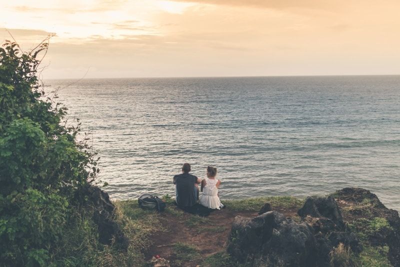 Mann und Frau sitzen auf dem Boden und schauen auf das Meer