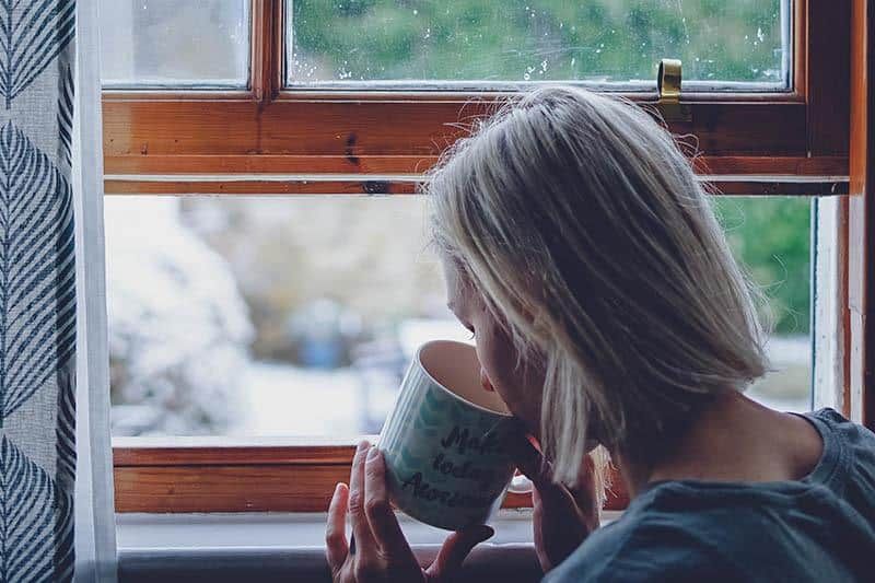 Frau trinkt Tee neben dem Fenster zu Hause