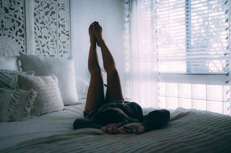 Frau liegt auf dem Bett und hebt ihre Beine