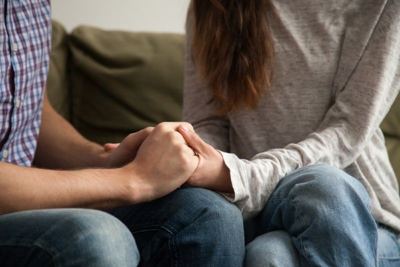 Mann und Frau halten sich an den Händen, während sie auf dem Sofa sitzen