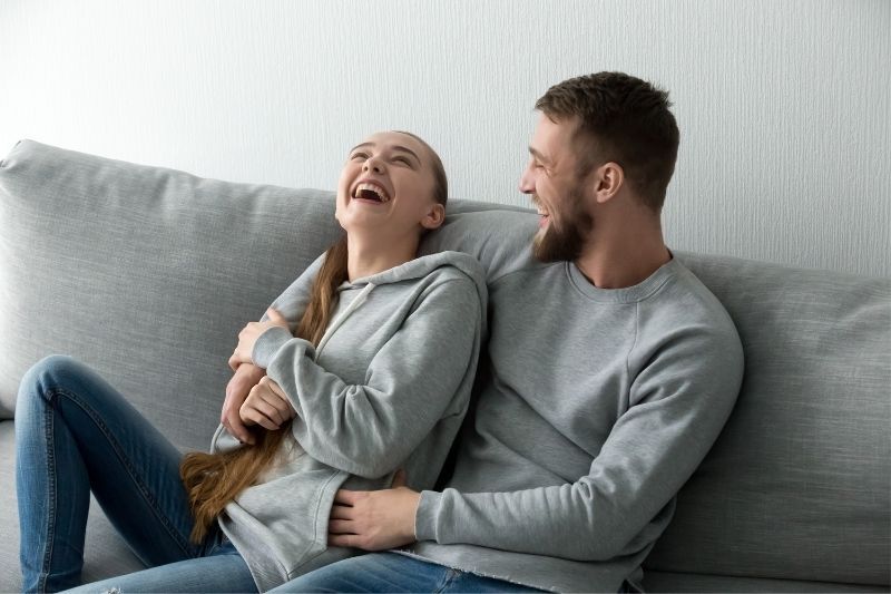 Fröhliches Paar, das sich auf der grauen Couch verbindet und graue Pullover trägt