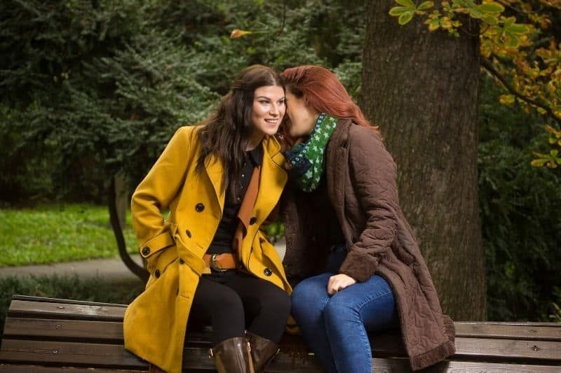 Zwei junge Freundinnen sitzen draußen und flüstern Gerüchte
