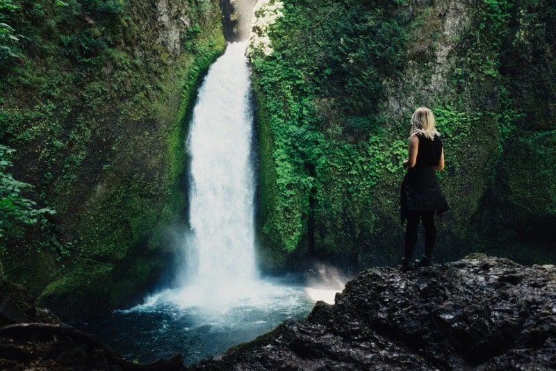Blonde Frau im schwarzen Top blickt auf den Wasserfall