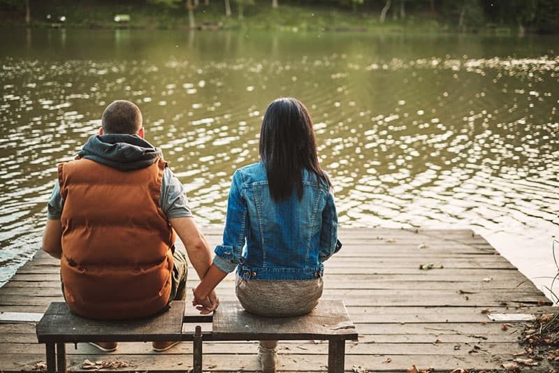 Glückliches Paar, das Händchen hält und am See sitzt