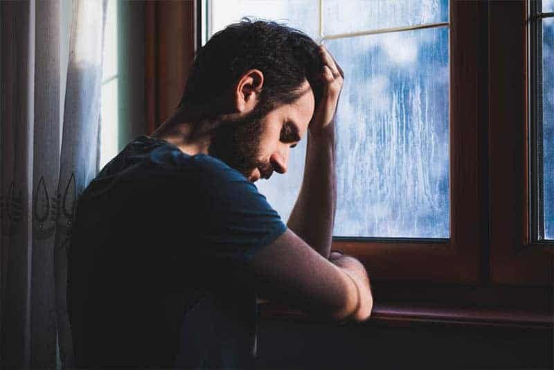 Deprimierter Mann hält seinen Kopf neben dem Fenster