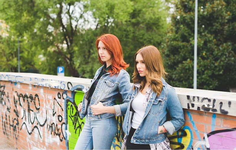 Kniefigur zweier Frauen in Jeansjacken und Jeans, die an der Wand lehnen
