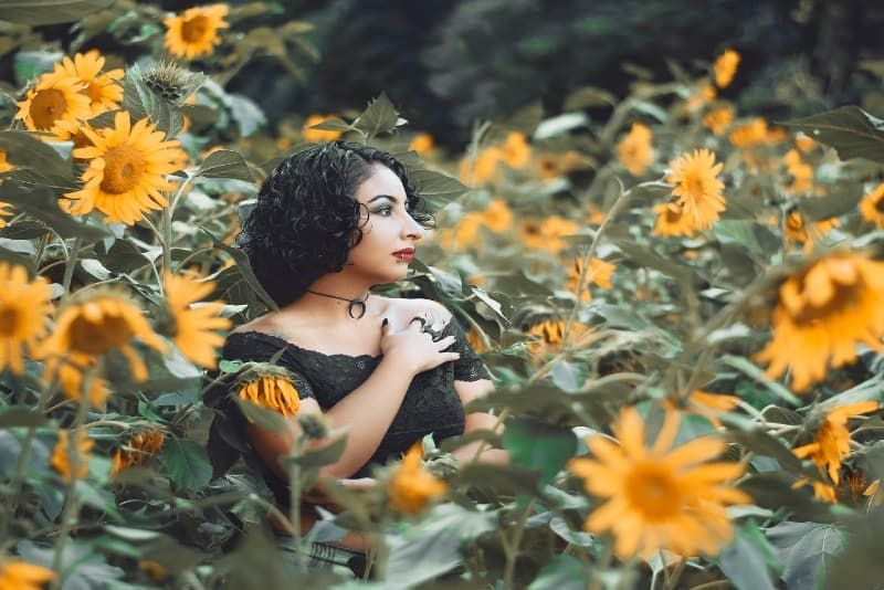 Frau im schwarzen Top steht umgeben von Sonnenblumen