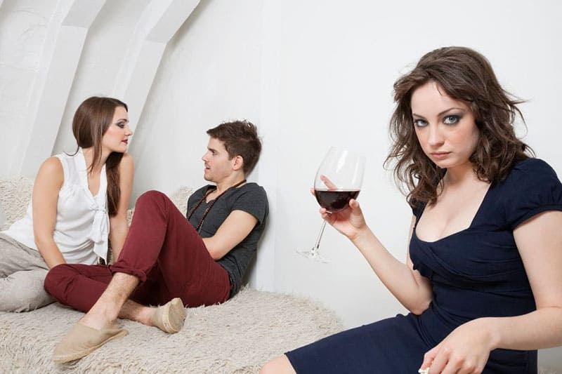 Frau hält ein Glas Wein und ist eifersüchtig auf die Liebenden in ihrer Nähe