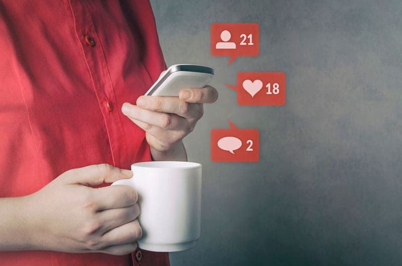 Person, die soziale Medien nutzt, bringt Tasse und Mobiltelefon mit ähnlichen Herz-Chat-Symbolen mit