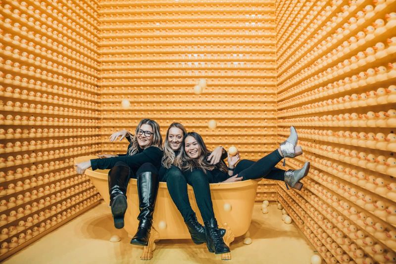 Drei Frauen lächeln, während sie in einer orangefarbenen Badewanne sitzen