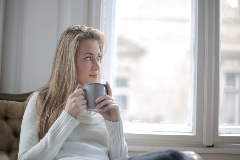 Frau trinkt Kaffee, während sie am Fenster sitzt