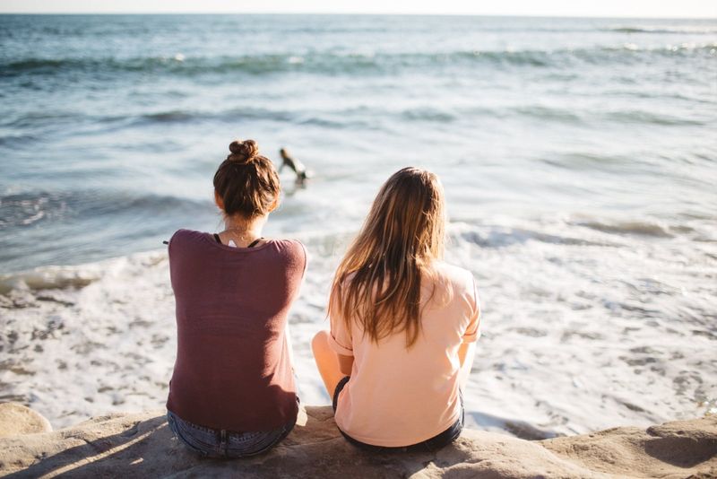 Zwei Frauen sitzen auf einer Klippe und schauen aufs Meer