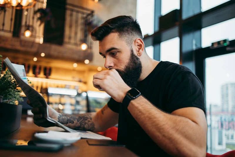 Tätowierter Mann sitzt im Café und trinkt Kaffee
