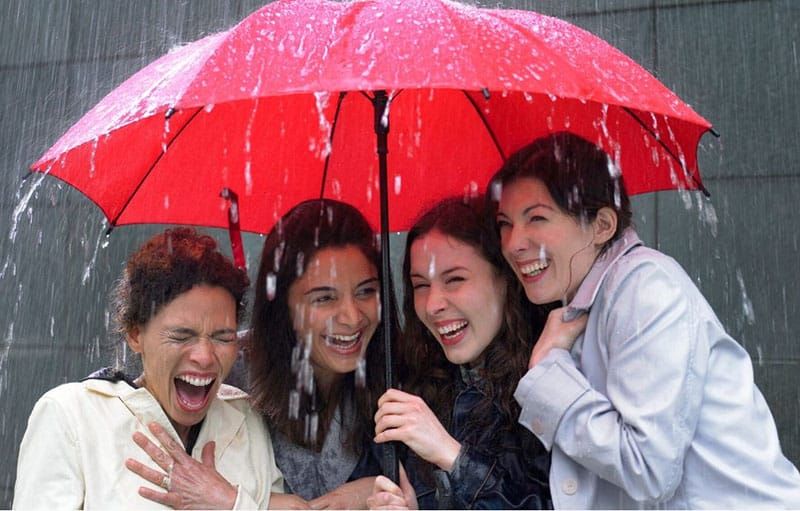 Vier Frauen teilen sich an einem regnerischen Tag unter einem roten Regenschirm