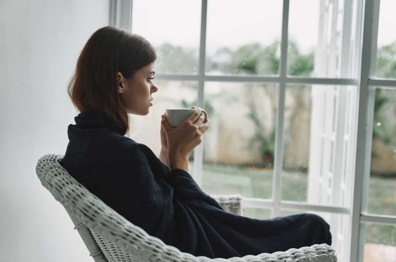 Frau sitzt am Fenster und trinkt Kaffee
