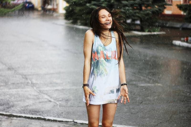 Frau in weißem Tanktop und Blau steht bei Regen auf der Straße
