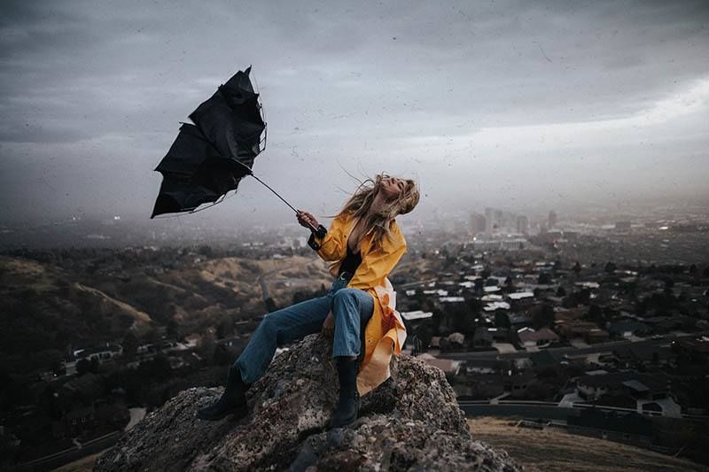 Frau hält Regenschirm, während sie draußen auf einem Felsen sitzt