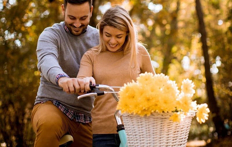 Paar teilt sich ein Fahrrad mit einem Blumenkorb im Park