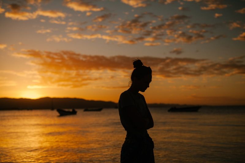 Traurige Frau, die bei Sonnenuntergang am Meer steht