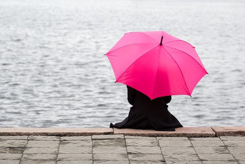 einsame frau, die mit rosa regenschirm im freien sitzt