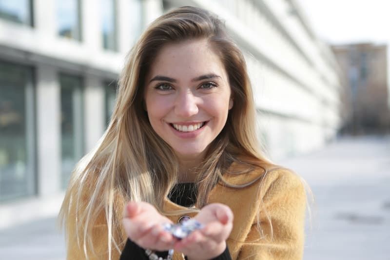 Frau im braunen Pullover lächelt und hält ein verschwommenes Bild von etwas in der Hand