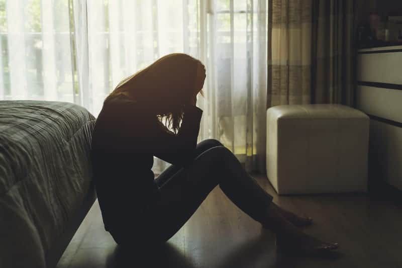 Seitenansicht einer depressiven Frau, die auf dem Boden sitzt