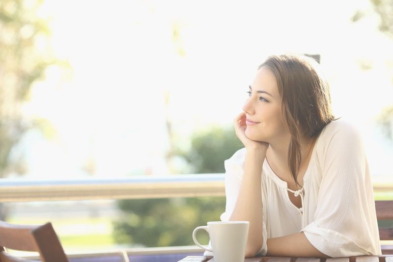glückliche nachdenkliche frau, die sich an glückliche momente erinnert, während sie im café sitzt