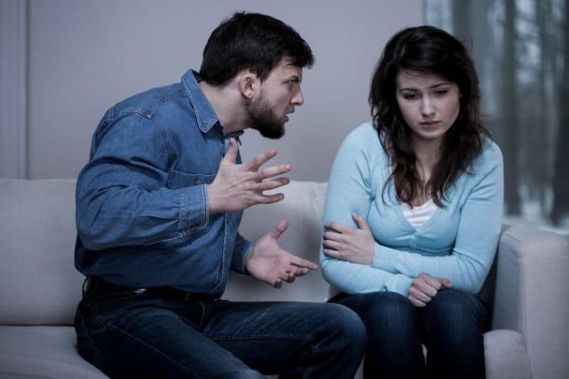 Traurige Frau und gewalttätiger Mann streiten auf der Couch im Wohnzimmer