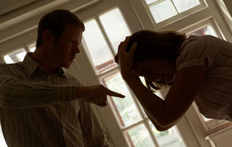 Mann wütend auf verärgerte Frau, die weint und ihren Kopf im Wohnzimmer hält