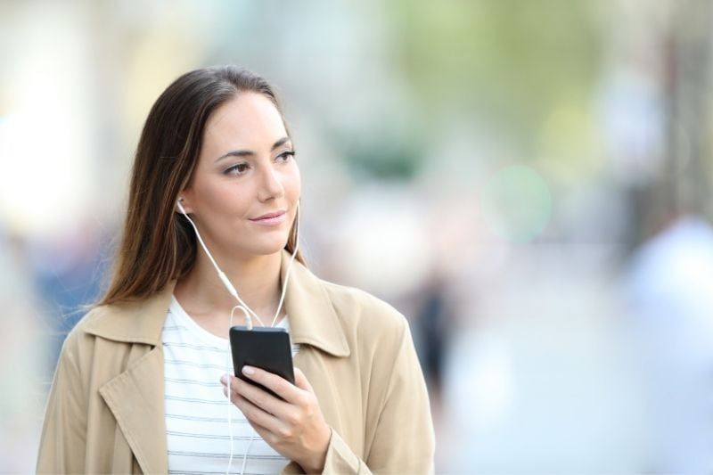 Nachdenkliche Frau hört Musik von ihrem Smartphone, während sie draußen geht