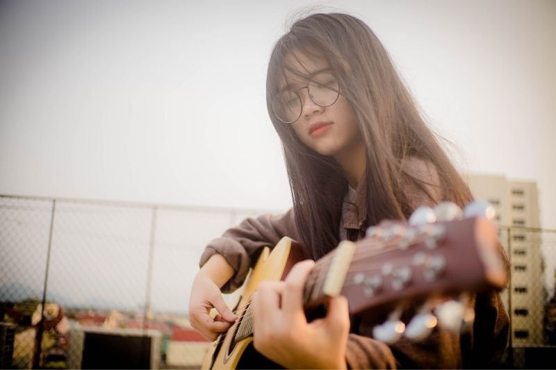 Asiatische Frau spielt Gitarre im Freien und trägt eine Brille