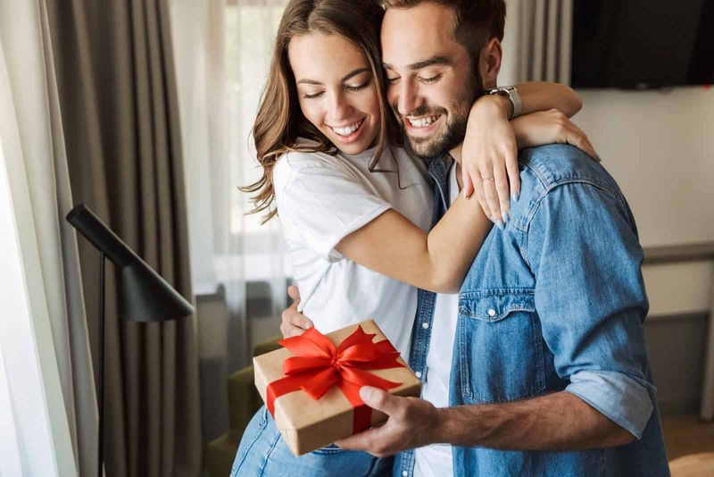 Lächelnder Mann und Frau umarmen sich, während er ein Geschenk hält