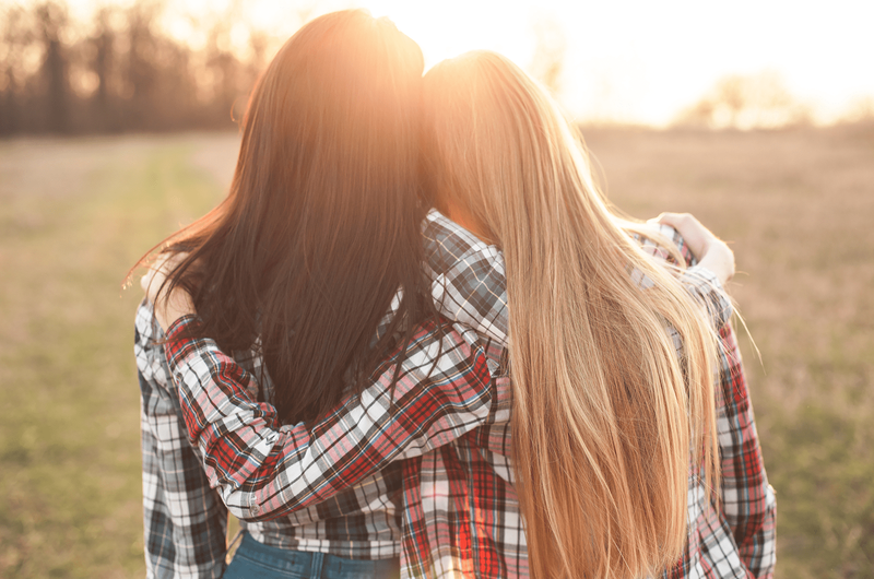 Zwei junge Frauen, die auf den Sonnenuntergang schauen und sich umarmen