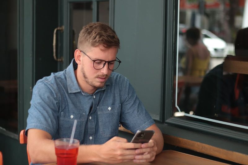 Mann mit Brille benutzt Smartphone, während er am Tisch sitzt