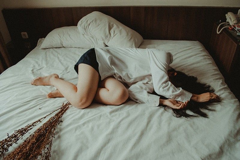 Frau liegt mit weißen Laken auf dem Bett