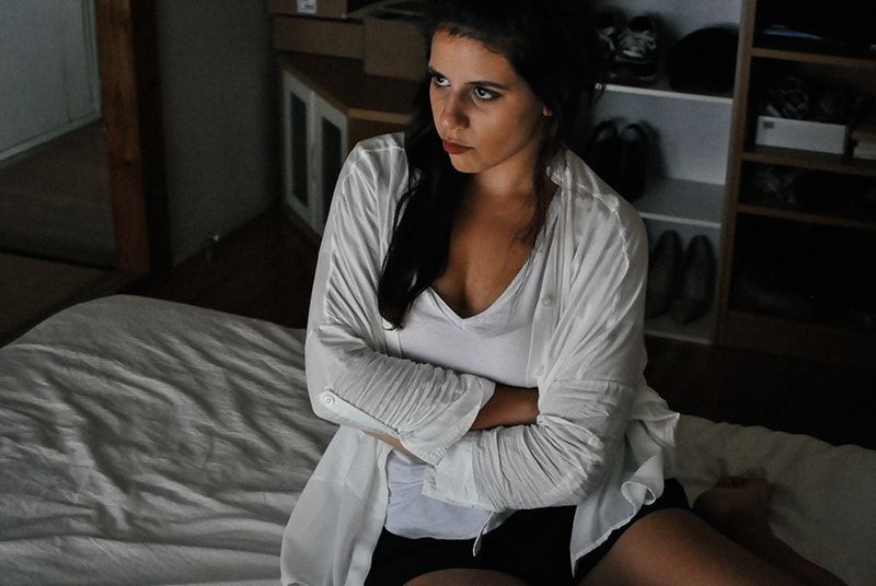 Frau mit weißer Strickjacke, während sie auf dem Bett sitzt