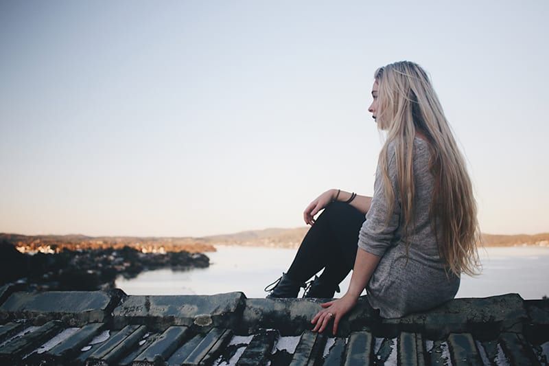 Frau sitzt auf grauem Dock in der Nähe von Gewässern