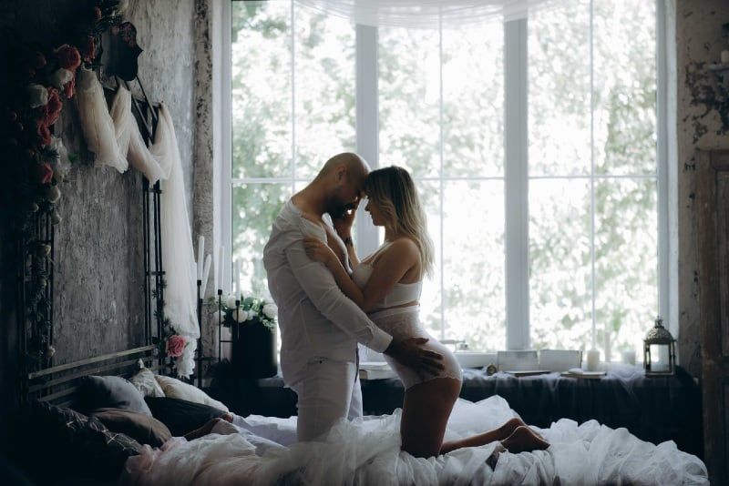 Mann und Frau knien auf dem Bett neben dem Fenster