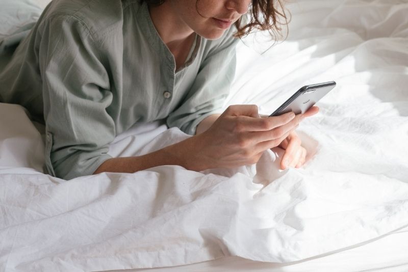 Frau, die Smartphone benutzt, während sie im Bett liegt