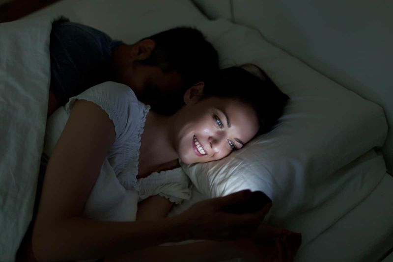 Frau telefoniert im Bett, während ihr Mann hinter ihr schläft
