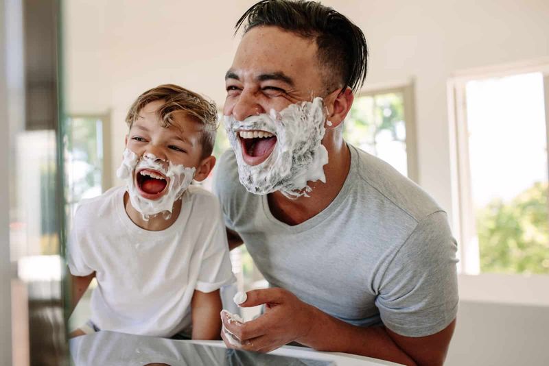 Vater und Sohn im Badezimmer mit Rasierschaum im Gesicht