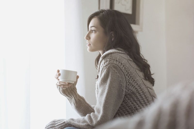 Seitenansicht einer nachdenklichen Frau, die Kaffee trinkt und die Fenster betrachtet