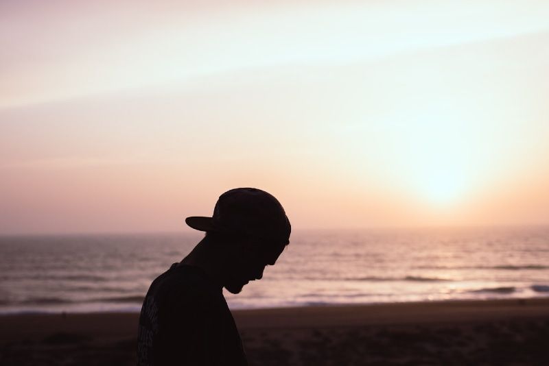 Mann mit Mütze steht bei Sonnenuntergang am Strand