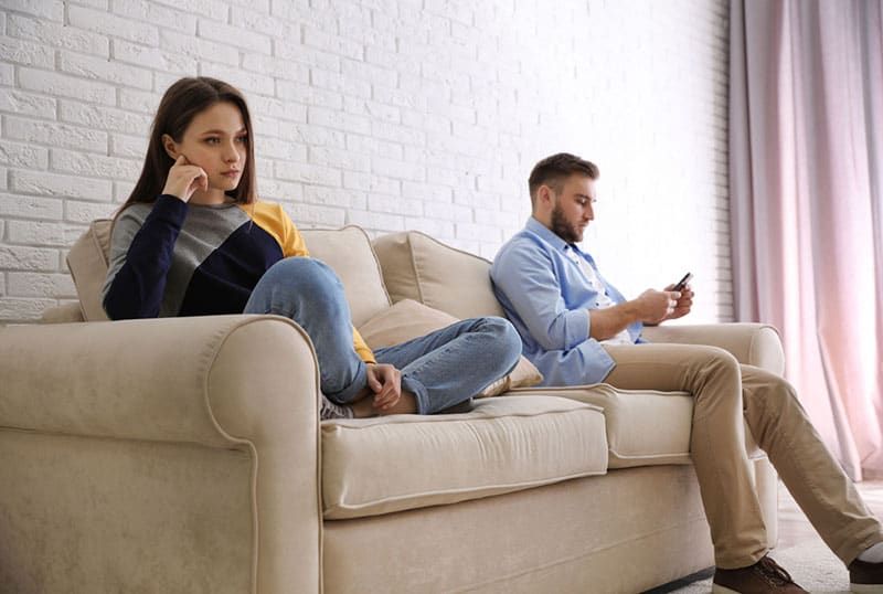 traurige Frau, die auf der Couch sitzt, während der Mann am Telefon tippt