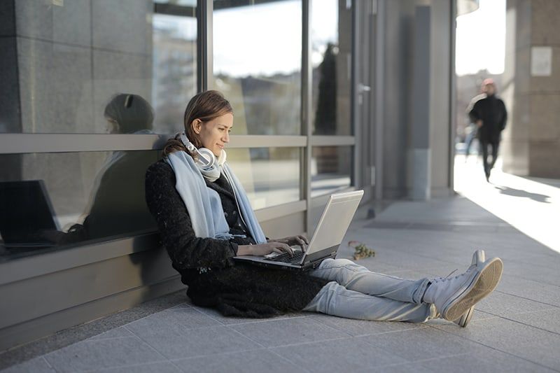 Frau sitzt auf grauem Betonboden und benutzt Laptop