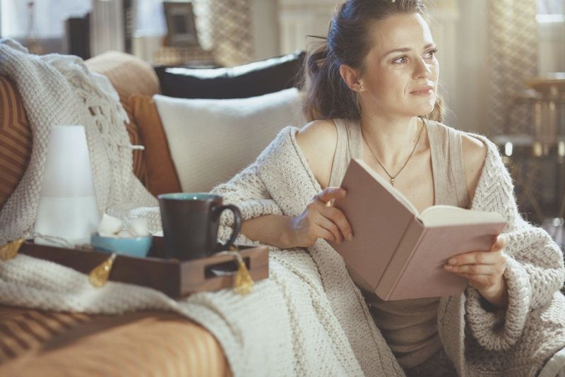Nachdenkliche Frau liest Buch in einem modernen Haus in einer Sommer-/Herbstsaison