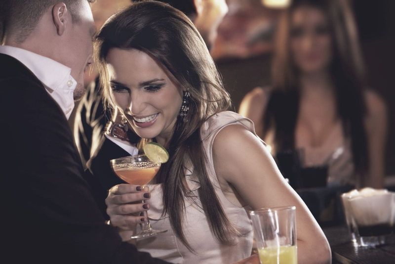 Mann flüstert Frau in einer Party/einem Club an, während er Wein trinkt